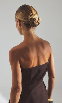 Pruun ilma rihmata kleit, millel on jalgu järgnev bodice ja volditud detail. Mudelil on madal kukk ja nähtav käe tätoveering. Sile nahk.