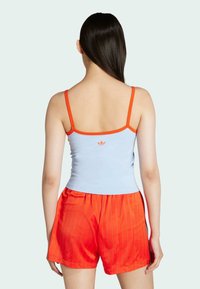 Ανοιχτό μπλε αμάνικο τοπ με πορτοκαλί λωρίδα, με κεντρικό λογότυπο, συνδυασμένο με κόκκινα κοντά παντελόνια με ρίγες. Μαλακό ύφασμα με εφαρμοστό σχέδιο.