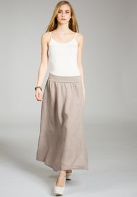 Leinen-Maxi-Rock in Hellbeige mit einem elastischen Bund und einem luftigen, lockeren Schnitt. Getragen mit einem weißen Tanktop und weißen Absätzen.