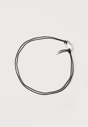 Collier en cuir noir à double brin avec un petit fermoir en boucle en argent martelé sur un fond clair uni.