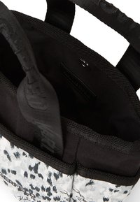 Tote bag with a black and white leopard print exterior, black fabric interior, sturdy straps, and top opening. Features a logo tag inside.