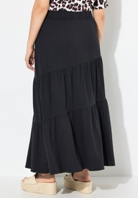 Gonna maxi nera a strati con vita elasticizzata e texture morbida, caratterizzata da un design fluido e volant sovrapposti all'orlo.