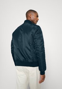 Giacca bomber blu navy con finitura satinata liscia, polsini e orlo a coste, dal taglio rilassato e design minimalista.