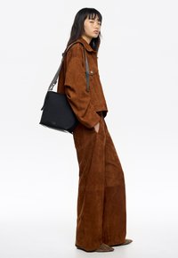 Chaqueta de ante color óxido y pantalones de pierna ancha, combinados con un bolso de tela negro con una correa gris. El conjunto tiene un acabado texturizado.