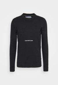 Maglione nero a maglia con maniche lunghe, collo rotondo e polsini a coste. Presenta il logo bianco "Calvin Klein Jeans" sul petto. Texture liscia.