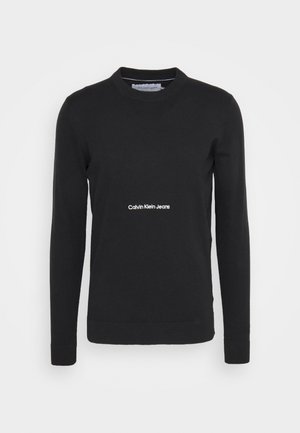 Suéter de punto negro con mangas largas, cuello redondo y puños acanalados. Presenta el logo blanco "Calvin Klein Jeans" en el pecho. Textura suave.