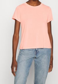 Světle růžové tričko s krátkým rukávem a kulatým výstřihem, vyrobené z měkké tkaniny. Má volný střih a hladkou texturu.