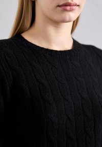 Schwarzer Strickpullover mit Zopfmuster, rundem Halsausschnitt und gerippten Abschlüssen. Die Textur wirkt weich und warm.