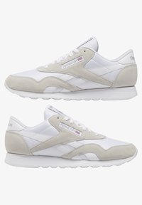 Bílé tenisky s nubukovými akcenty, s nízkým střihem, šněrováním, gumovou podrážkou a značkou Reebok na boku.