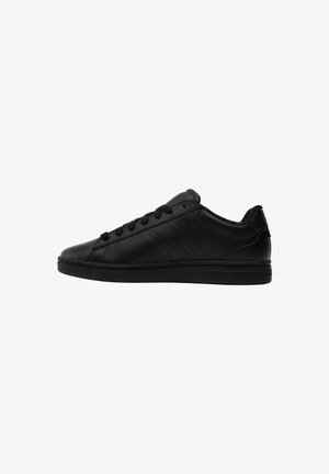 Zwarte lage leren sneaker met zwarte veters en een platte rubberen zool, van opzij getoond tegen een witte achtergrond.