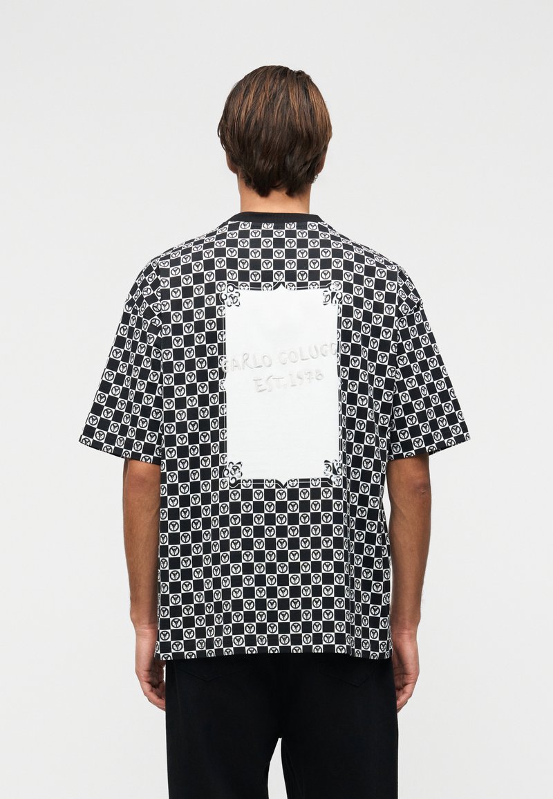 Άνδρας που φοράει πουκάμισο με κοντά μανίκια σε ασπρόμαυρο καρό σχέδιο με κυκλικά λογότυπα και ένα μεγάλο λευκό ορθογώνιο μπαλώμα στην πλάτη.