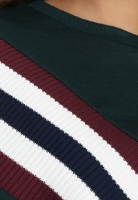 Prenda de color verde oscuro con un patrón de rayas diagonales y textura acanalada en colores marrón, blanco y azul marino.