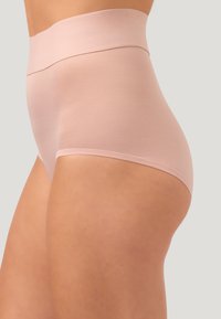 Slip in nude colore a vita alta e senza cuciture indossato da una persona, mostrando una vestibilità fluida e una copertura sulle anche e sulla vita su uno sfondo neutro.