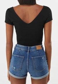 Svart ribbad kortärmad topp med V-ringning, kombinerad med blå denimshorts med uppvikta kanter och synliga bakfickor.