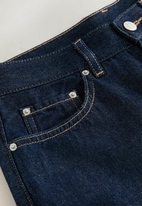 Dunkelblaue Jeans aus Denim mit einer Vordertasche, silbernen Nieten und kontrastierenden orangefarbenen Nähten an den Kanten.