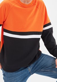Felpa arancione e nera con strisce bianche, collo rotondo e maniche raglan. Materiale morbido, vestibilità casual.