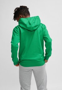 Grøn hætte-sweatshirt med en glat tekstur, featuring en foran kangaroo lomme og ribbede manchetter. Sammen med lysegrå sweatpants.