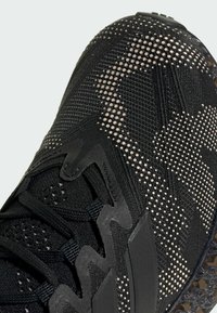 Black athletic shoe featuring a textured fabric upper with a dotted pattern, reinforced lacing, and a durable rubber sole.