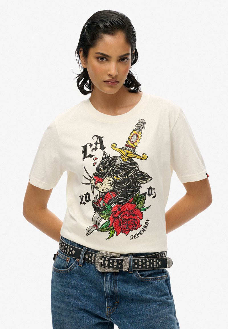 Wit katoenen T-shirt met een grafisch ontwerp van een zwarte kat met een zwaard en rode rozen, naast textelementen in felle kleuren.