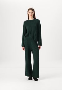 Dark green cable knit sweater and matching wide-leg pants, featuring a relaxed fit, ribbed texture, and long sleeves.