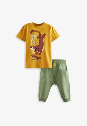 T-shirt en coton jaune avec un graphique de tigre et le texte "SKATER" ; associé à un pantalon de jogging vert avec taille élastique et poches latérales.