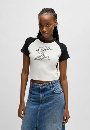 Kort topp med vit kropp och svarta raglanärmar, rolig pizzagrafik och text; matchad med en midjelång denimkjol.