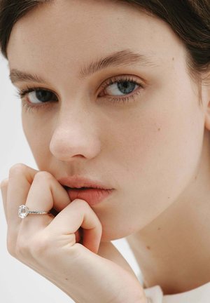 Joven con ojos azules apoyando la barbilla en la mano, lleva un gran anillo de diamantes rectangular en el dedo anular.