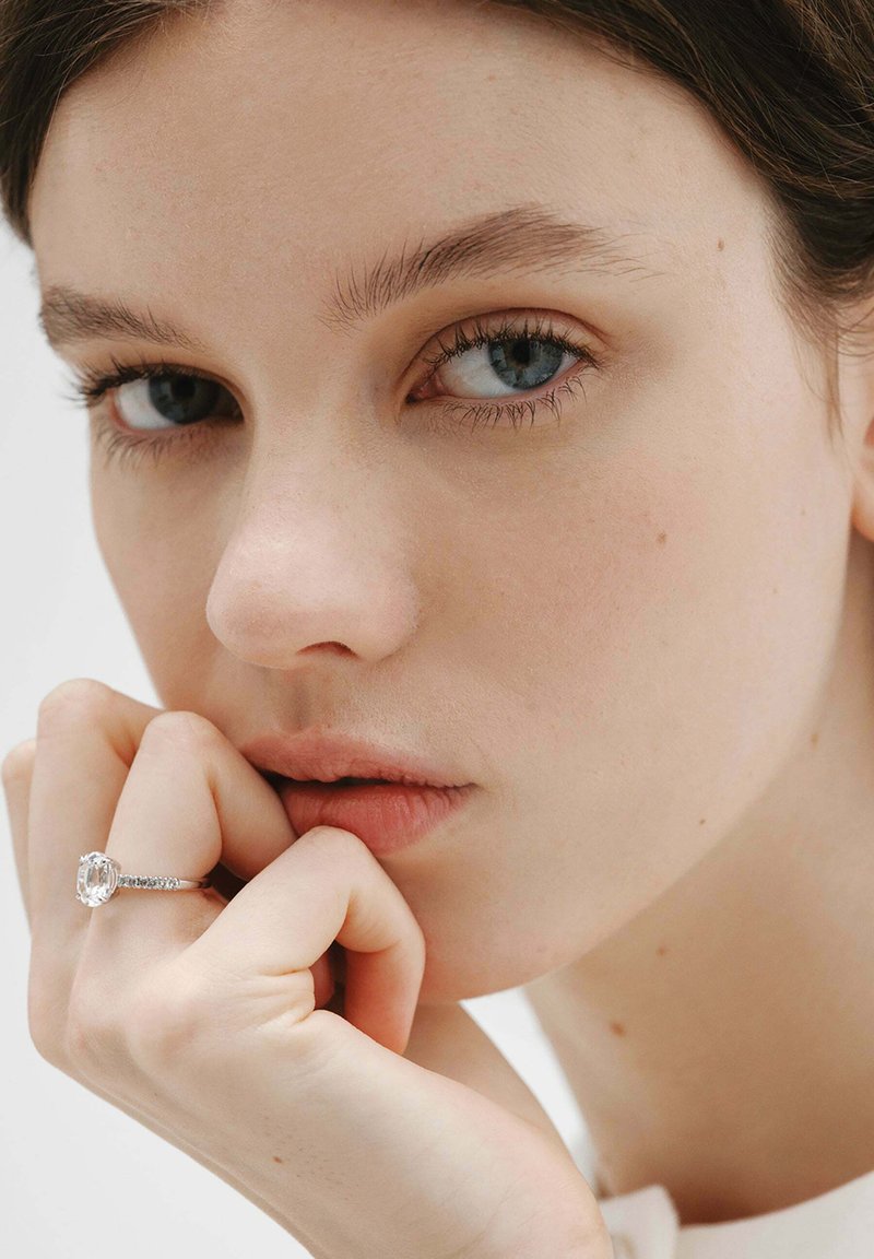 Joven con ojos azules apoyando la barbilla en la mano, lleva un gran anillo de diamantes rectangular en el dedo anular.