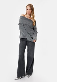 Grauer schulterfreier Pullover mit geripptem Kragen, kombiniert mit dunkelblauen weiten Jeans und glänzenden silbernen spitzen High Heels.