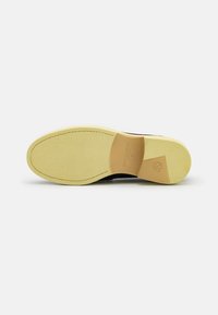 Schwarze Schuhsohle mit einer strukturierten gelben Gummisohle, einem gebogenen Absatz und einem beigen Akzent am Absatz mit geprägt Branddetail.