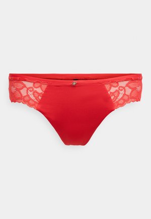 Tanga vermelha com lingerie, apresentando um tecido frontal liso e detalhes elaborados em renda nas laterais, realçados com um pequeno adorno metálico.
