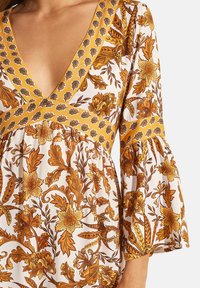 Robe florale avec un décolleté en V profond, des manches évasées et une bande d'accent jaune, ornée de motifs botaniques orange et marron sur fond blanc.