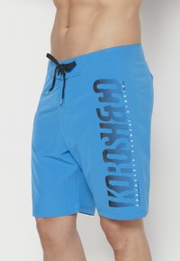 Shorts de baño azules con un diseño gráfico negro a lo largo del costado, hechos de una tela ligera, con una cintura ajustable con cordón.