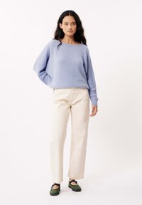 Pull en maille texturée bleu clair avec une coupe ample, associé à un pantalon droit couleur crème et des mocassins verts avec une semelle noire.