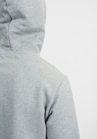 Felpa grigia con cappuccio realizzata in morbido tessuto misto cotone, caratterizzata da un design semplice con una vista posteriore che mostra il cappuccio e le cuciture.