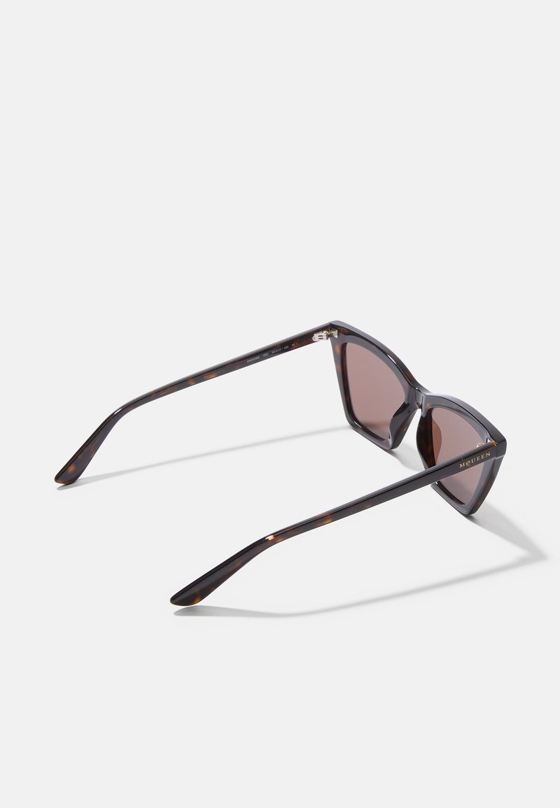 Occhiali da sole tartaruga marrone con montatura angolare, lenti marroni e aste eleganti e affusolate decorate con un logo dorato.