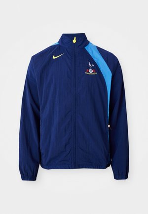 Marinefarbene Windjacke mit blauen Seitenakzenten, hohem Kragen und Nike-Logo. Ausgestattet mit elastischen Bündchen und einem Kordelzug am Saum.