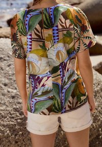 Chemise à manches courtes avec un motif floral et géométrique multicolore, fabriquée en tissu léger, avec un détail en forme de trou de serrure au dos.