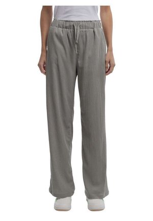 Personne portant un pantalon gris texturé ample avec une taille élastique et un cordon, assorti à des baskets blanches et un haut blanc.