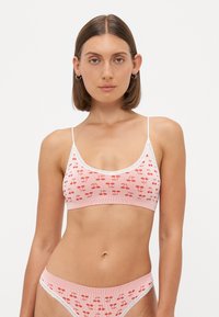 Svijetloružičasti rebrasti bralet sa uzorkom crvenih trešanja, čipkastim obrubom i prilagodljivim trakama, uparen s bikini donjim dijelom ukrašenim čipkom.