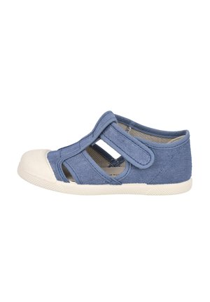 Zapatilla de lona azul con recortes y una puntera de goma blanca. Presenta correas de Velcro para facilitar su uso. Parte superior texturizada y suela flexible.