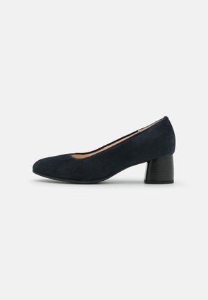 Marineblå ruskinds pumpe med rund tå, lav blokhæl og et minimalistisk design. Glat tekstur; indersiden har et lyst for.