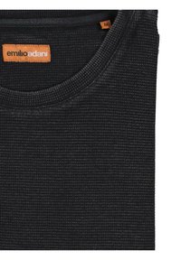 Schwarzes, strukturiertes Tanktop mit einem runden Ausschnitt. Verfügt über ein oranges Markenlabel in der Nähe des Kragens und ein sichtbares Größenetikett im Nackenbereich.