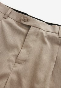 Beige broek met riemlussen, een knoopsluiting en een verborgen rits, weergegeven op een witte achtergrond.