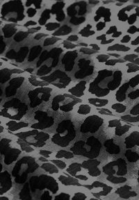 Miękka tkanina z czarnym i ciemnoszarym wzorem w cętki lamparta, ukazująca fałdy i teksturę na powierzchni.