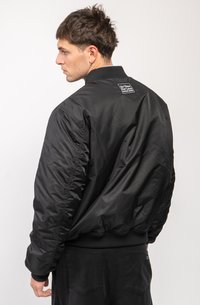 Black bomber jacket with a ribbed collar, elastic cuffs, and a branded patch on the back. The fabric appears smooth and slightly shiny.