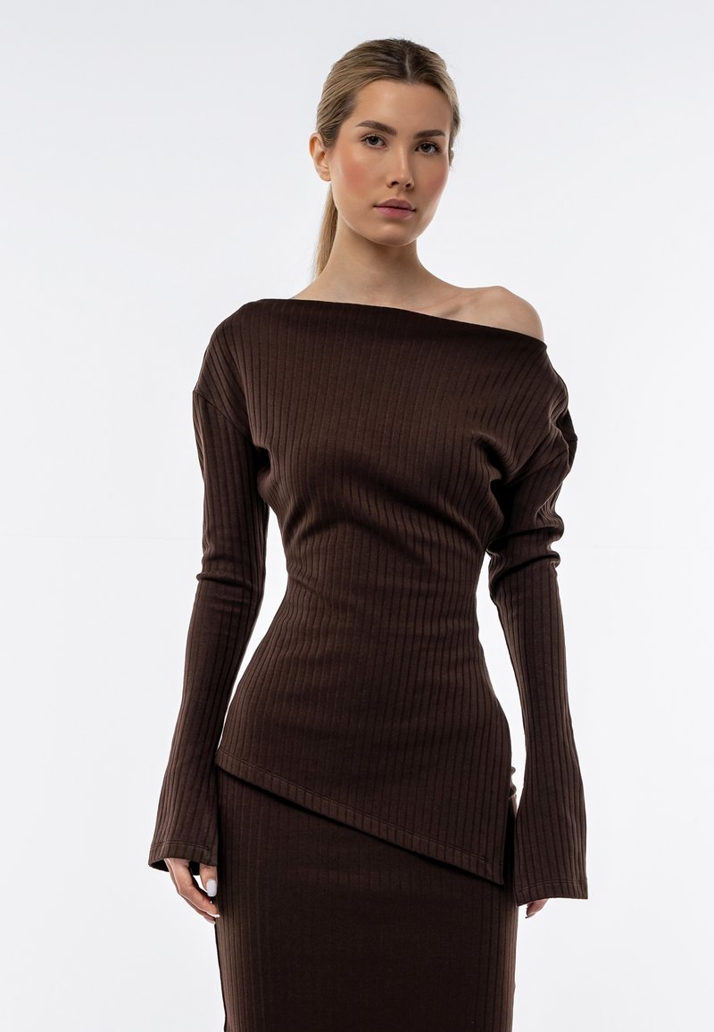 Top marrone a coste con spalle scoperte e maniche lunghe, caratterizzato da un orlo leggermente asimmetrico e un design aderente che si modella sul corpo.