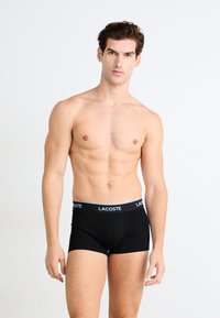 Zwarte bokser shorts met een blauw-witte tailleband waarop het 'LACOSTE' logo staat, gemaakt van zachte stof, met een aansluitend ontwerp en een lengte tot halverwege de bovenbenen.