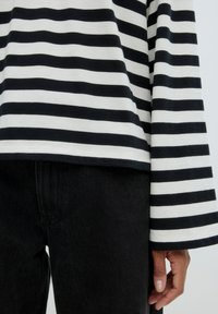 Zwart-witte gestreepte longsleeve top met wijde mouwen, gecombineerd met zwarte denim broek. Stof lijkt zacht met een gladde textuur.