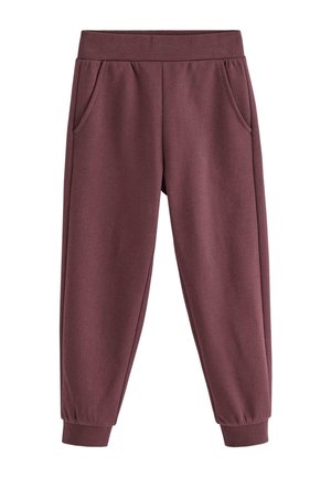 Barn iført mørkelilla joggingbukser, hvid langærmet skjorte med sorte polkaprikker og beige sneakers med snørebånd.